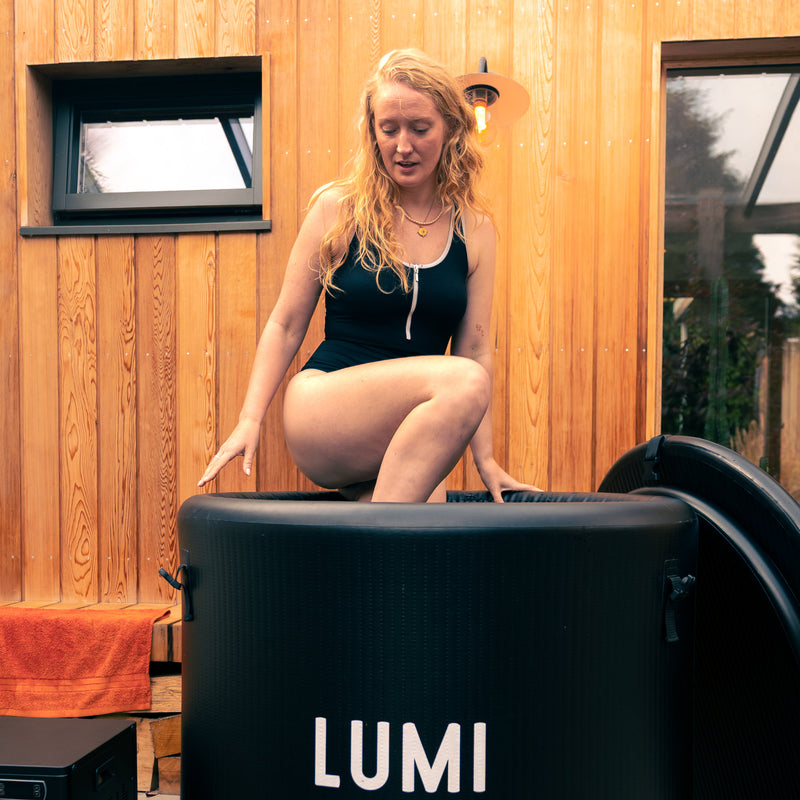 Woman with blond curly hair wearing a black swimsuit stepping into the LUMI Pro 8 ice barrel.