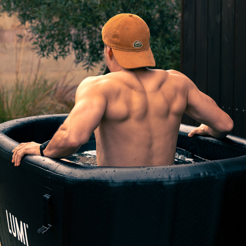 Rear view of a man wearing a baseball cap, sitting in the LUMI Pro Duo ice bath.