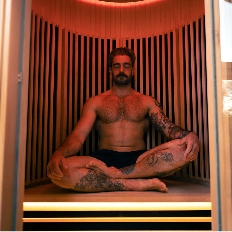 Photo of a man sitting crossed legged in the LUMI Sauna PRO Duo infrared wooden sauna.