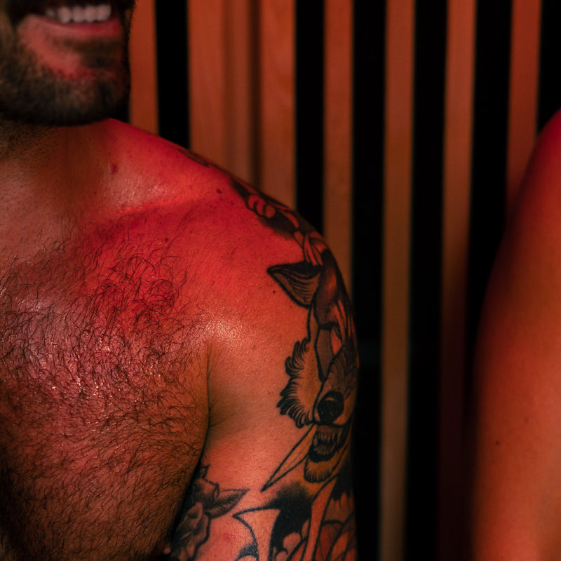 Closup of a sweaty man with a tattoos on his shoulder, sat next to a woman in the LUMI Sauna PRO.