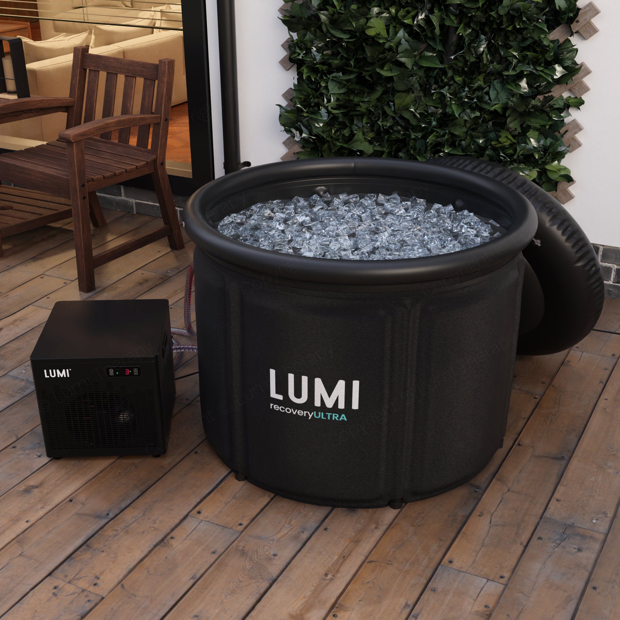 Recovery Ultra and Cube Chiller system by LUMI shown in an indoor setting, featuring a large black portable ice bath filled with ice cubes alongside a compact black cooling unit, positioned on wooden flooring with decorative greenery in the background.