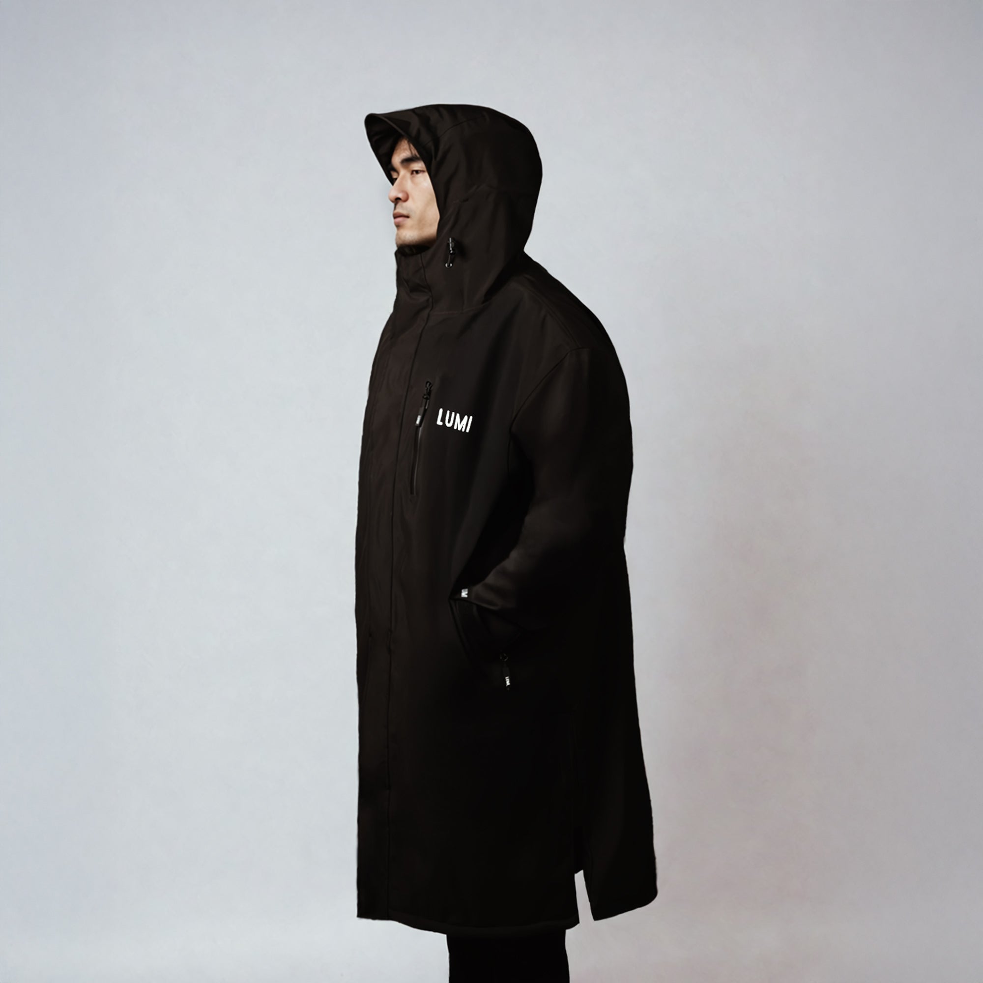 Side profile of a person wearing the LUMI Robe PRO DUO in black, highlighting its sleek design, waterproof outer shell, and pull-cord hood for outdoor use