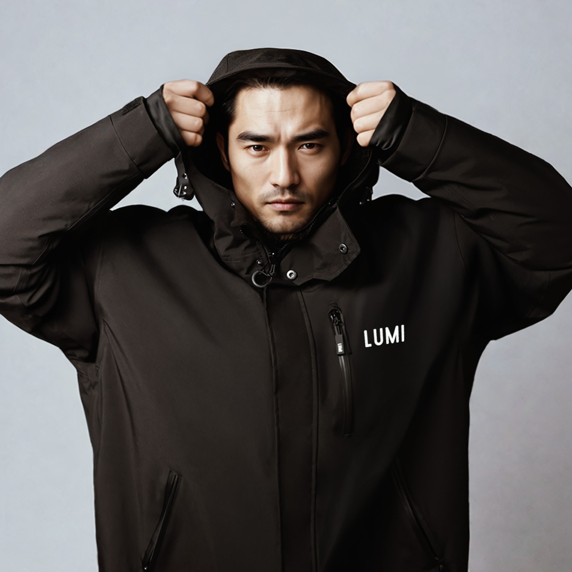 PRO DUO Changing Robe in Black - Model wearing stylish black waterproof robe with high collar and hood, featuring LUMI logo and zippered chest pocket against grey background. Showcasing protective design and premium outerwear functionality.