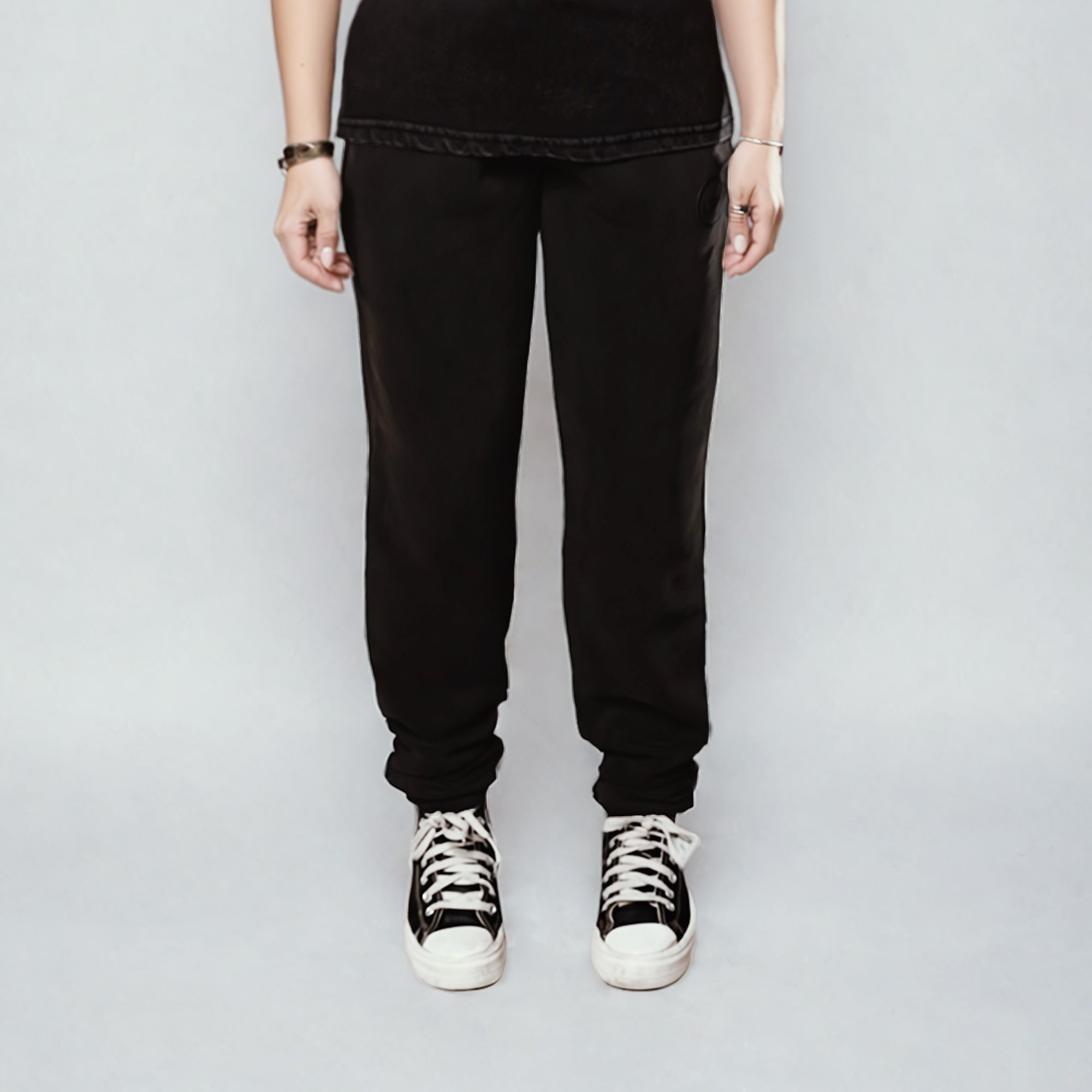 Women's LUX Sweatpants Black Wash shown from waist down, featuring relaxed-fit silhouette with elastic cuffs, paired with black and white sneakers. Sweatpants display a comfortable cotton-blend fabric in black wash finish against light grey background.