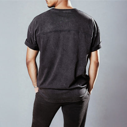 Men's LUX Oversized T-Shirt Black Wash shown from back view, featuring premium panelled construction with rolled sleeves and a relaxed fit. The black washed cotton fabric creates a vintage-inspired aesthetic against a light grey background.