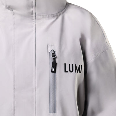 PRO DUO Changing Robe in grey with LUMI logo, featuring a waterproof zipper pocket detail and high-quality matte finish. Close-up view of upper shoulder and chest area showing premium construction and Nordic-inspired design.