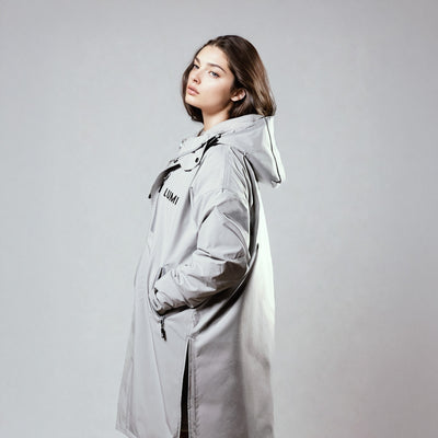 PRO DUO Changing Robe in grey shown as a stylish Nordic-inspired jacket with hood, featuring waterproof exterior and side zipper details against a neutral studio background. Demonstrates sleek silhouette and practical design elements of the changing robe.