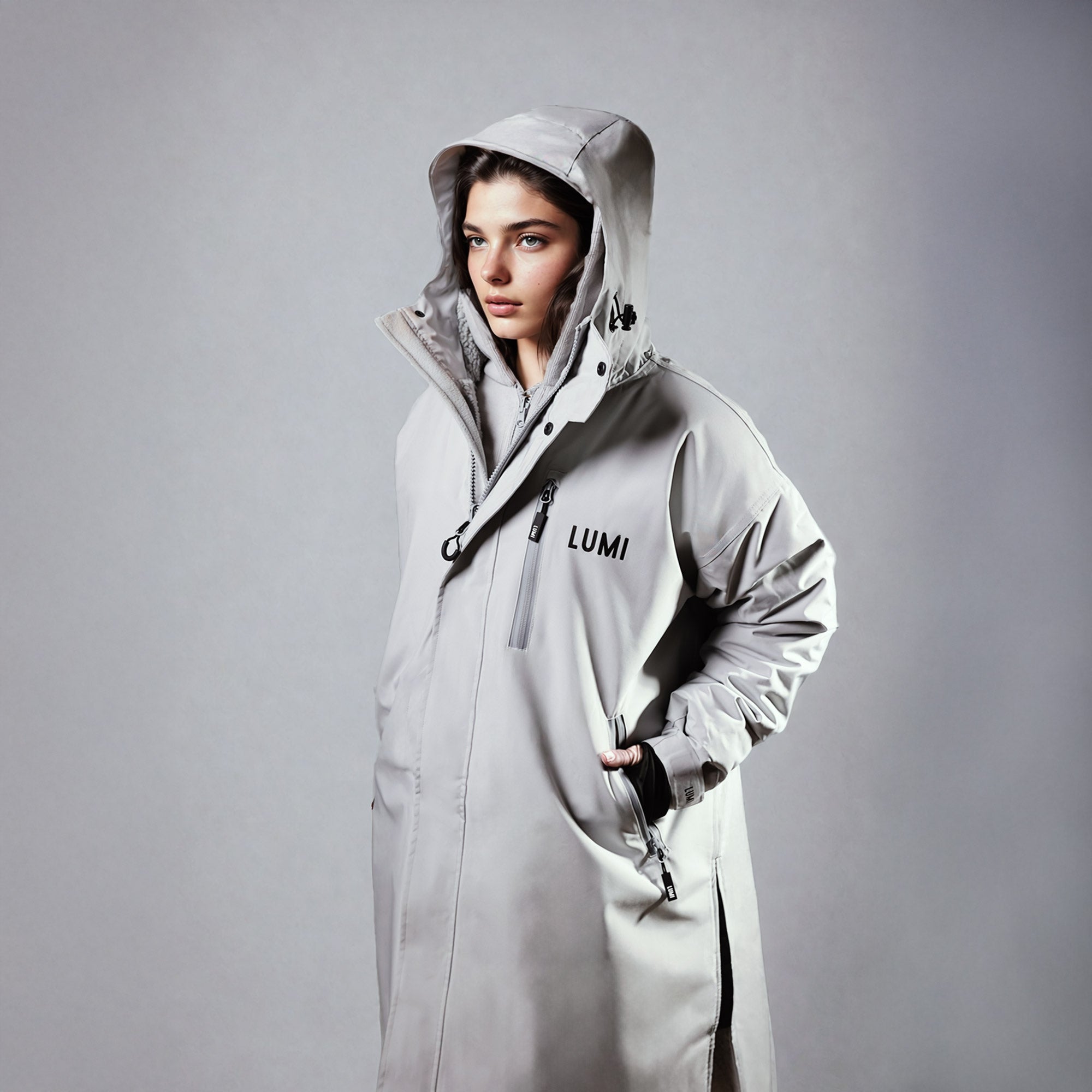 A person wearing the PRO DUO Changing Robe in Grey, showcasing its waterproof exterior, adjustable hood, and modern Nordic design. The robe features LUMI branding, multiple zippers, and a sleek silhouette against a neutral studio background.