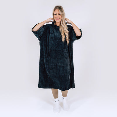 LUMI Towel Poncho shown as an oversized hooded robe in luxurious black cotton fabric, featuring roomy design with front pocket, modeled against white background, displaying full-length coverage and comfortable fit
