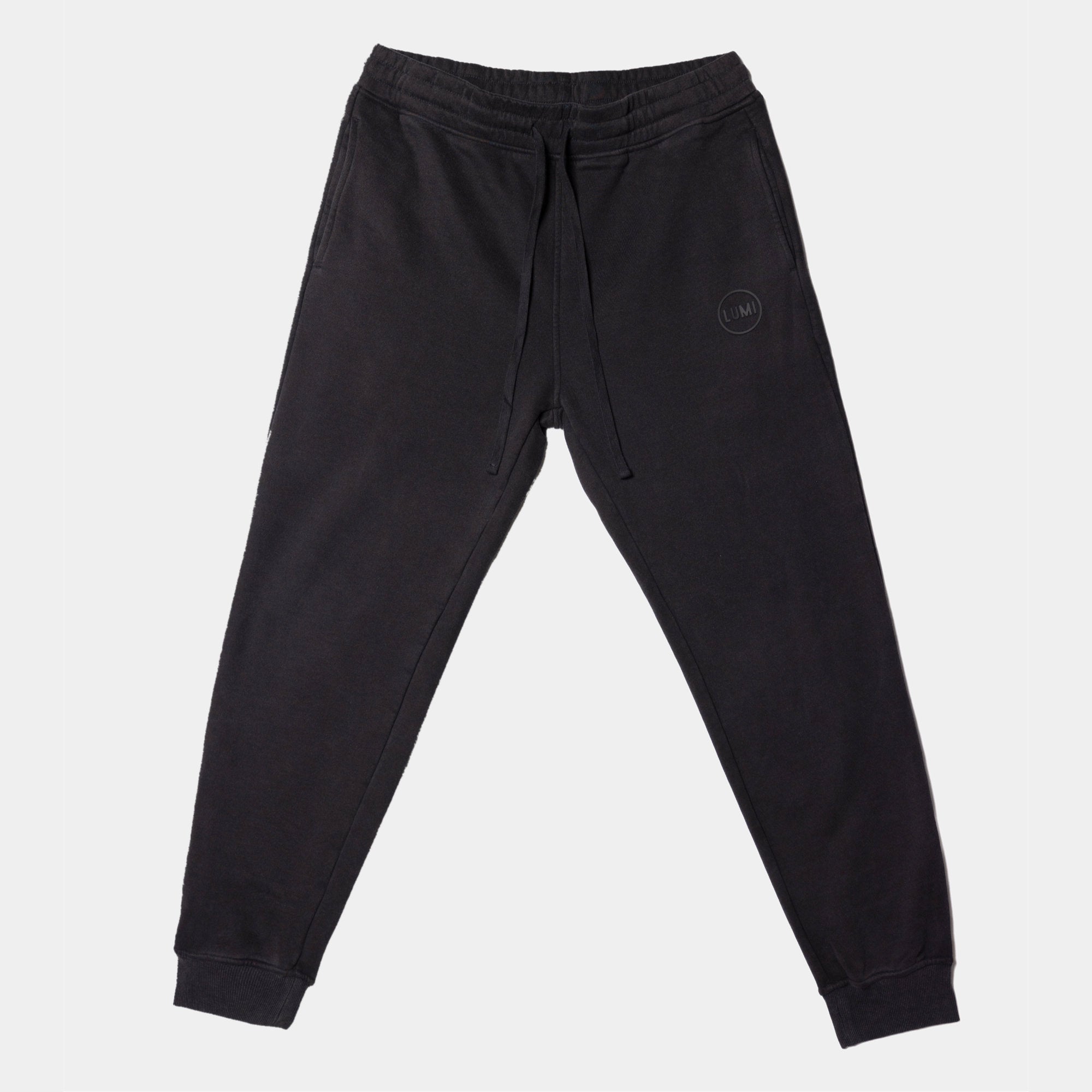 Men's LUX Sweatpants Black Wash featuring relaxed-fit design in black wash cotton-polyester blend, with elasticated waistband, cuffed ankles, and subtle raised rubber LUMI logo on leg. Displayed flat against white background showcasing full-length view.