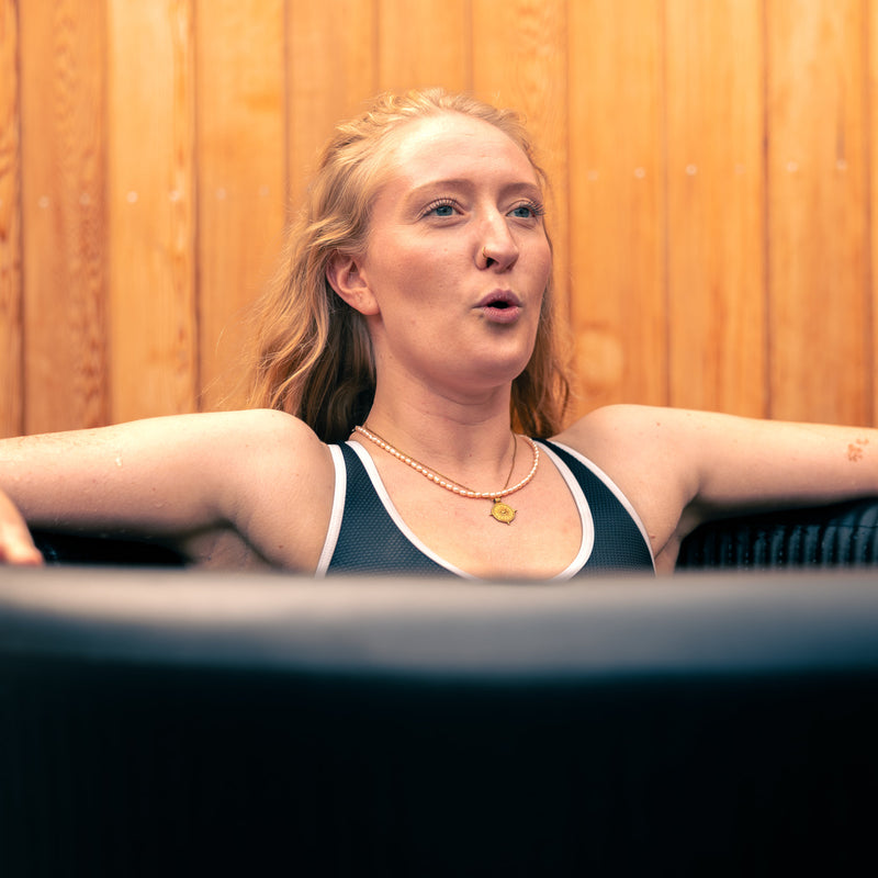 Woman with blonde hair sat in the LUMI Pro 8 ice barrel, using breathing technique during cold water therapy.