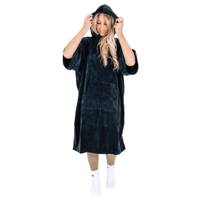 Woman wearing black LUMI Towel Poncho Changing Robe from Cold Club Starter Set adjusting hood and smiling