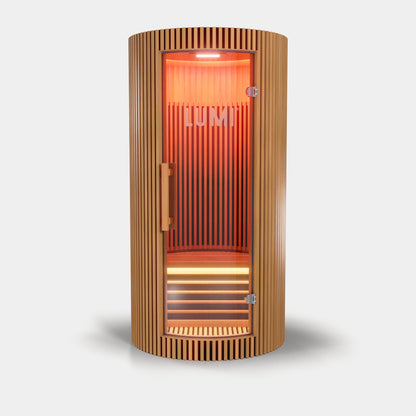 LUMI Sauna PRO, a modern cylindrical infrared sauna with premium Hemlock wood slats, featuring a curved glass door and glowing red interior lighting, showcasing Scandinavian design with warm ambient illumination against a white background