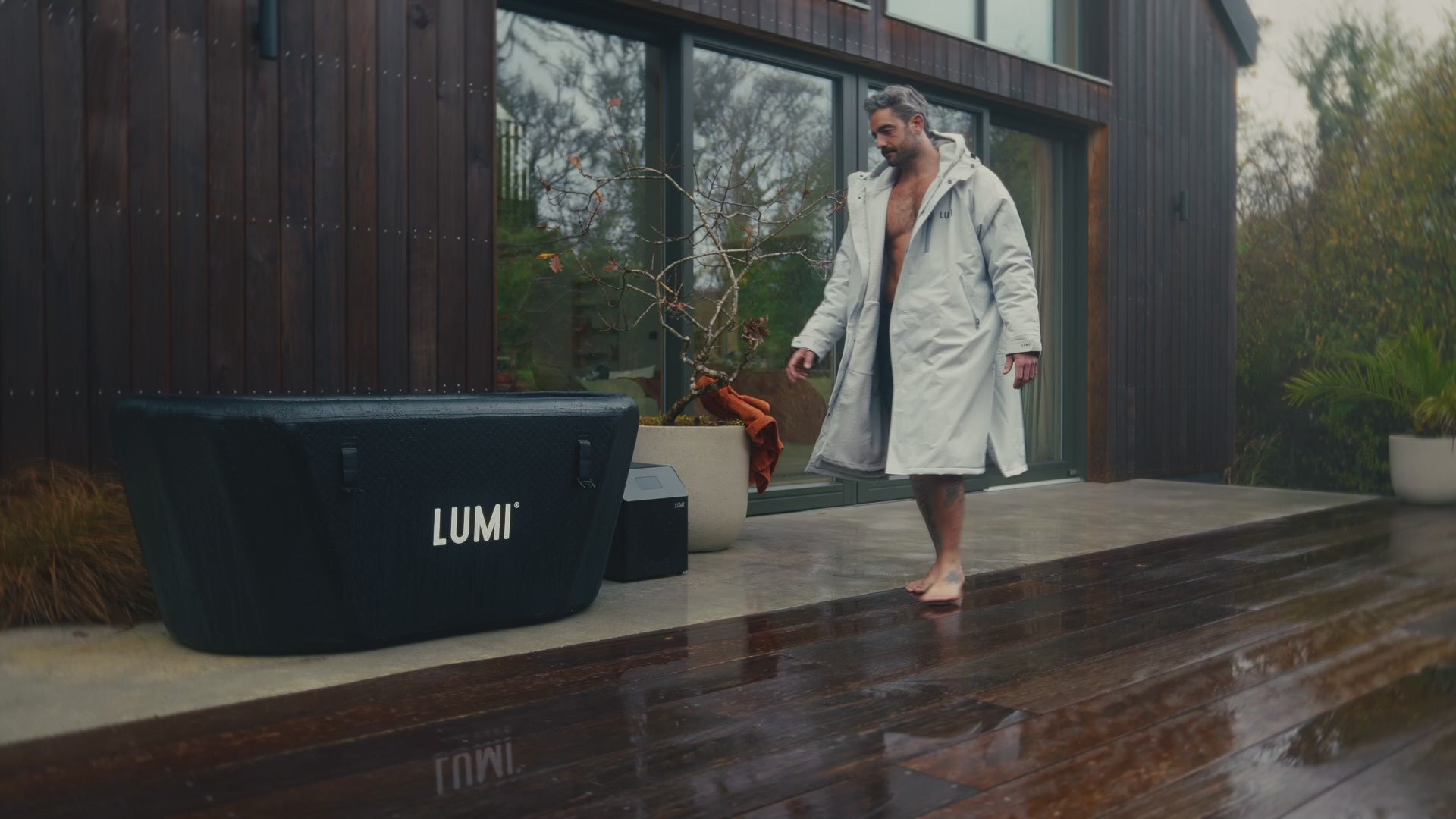 Load video: Video of a man wearing the LUMI RobePRO and swimshorts, getting in the LUMI Pro Duo ice bath, focused on cold water recovery.